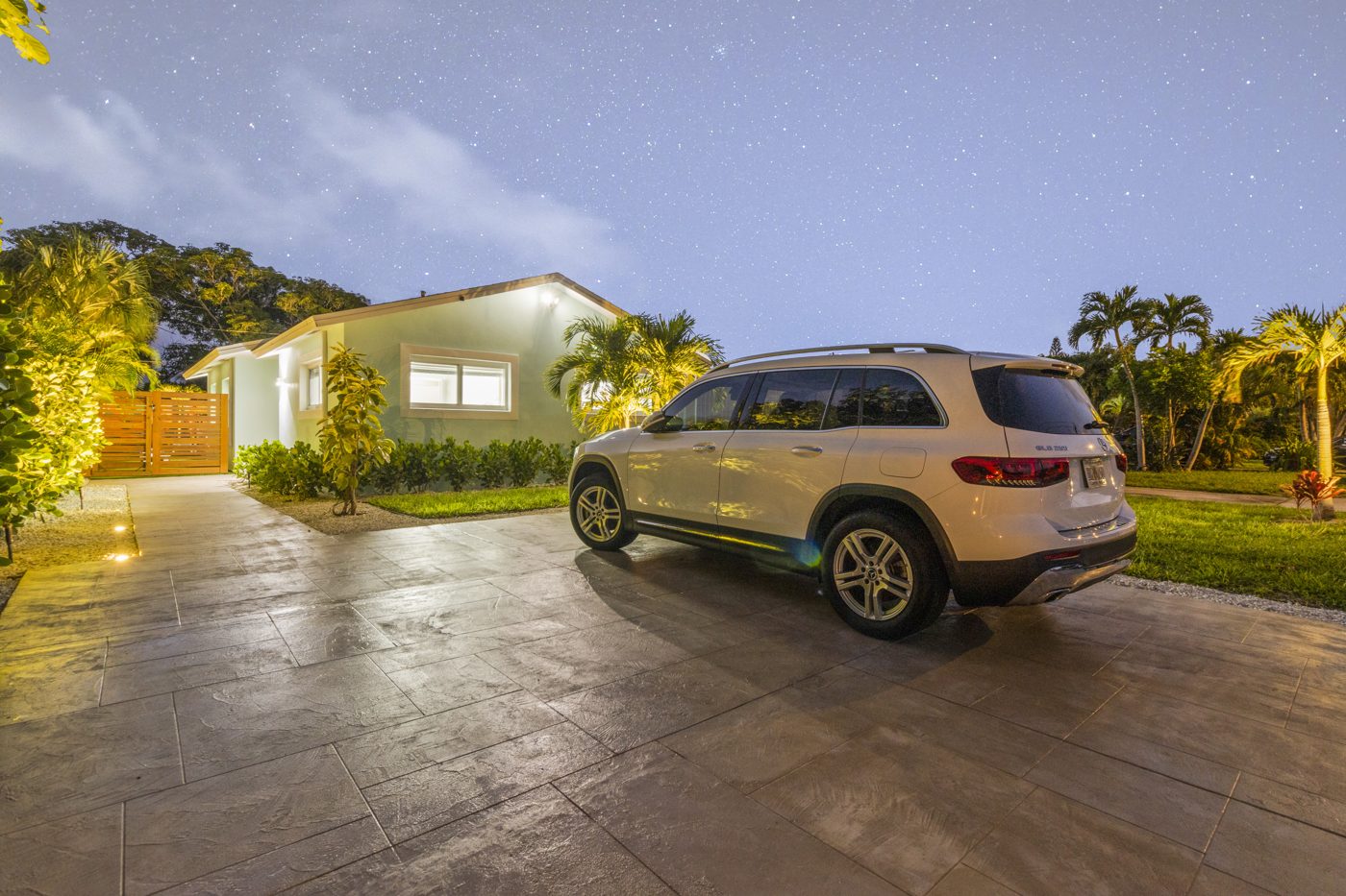 The house after: renovated exterior, new lighting and a paved driveway at dusk