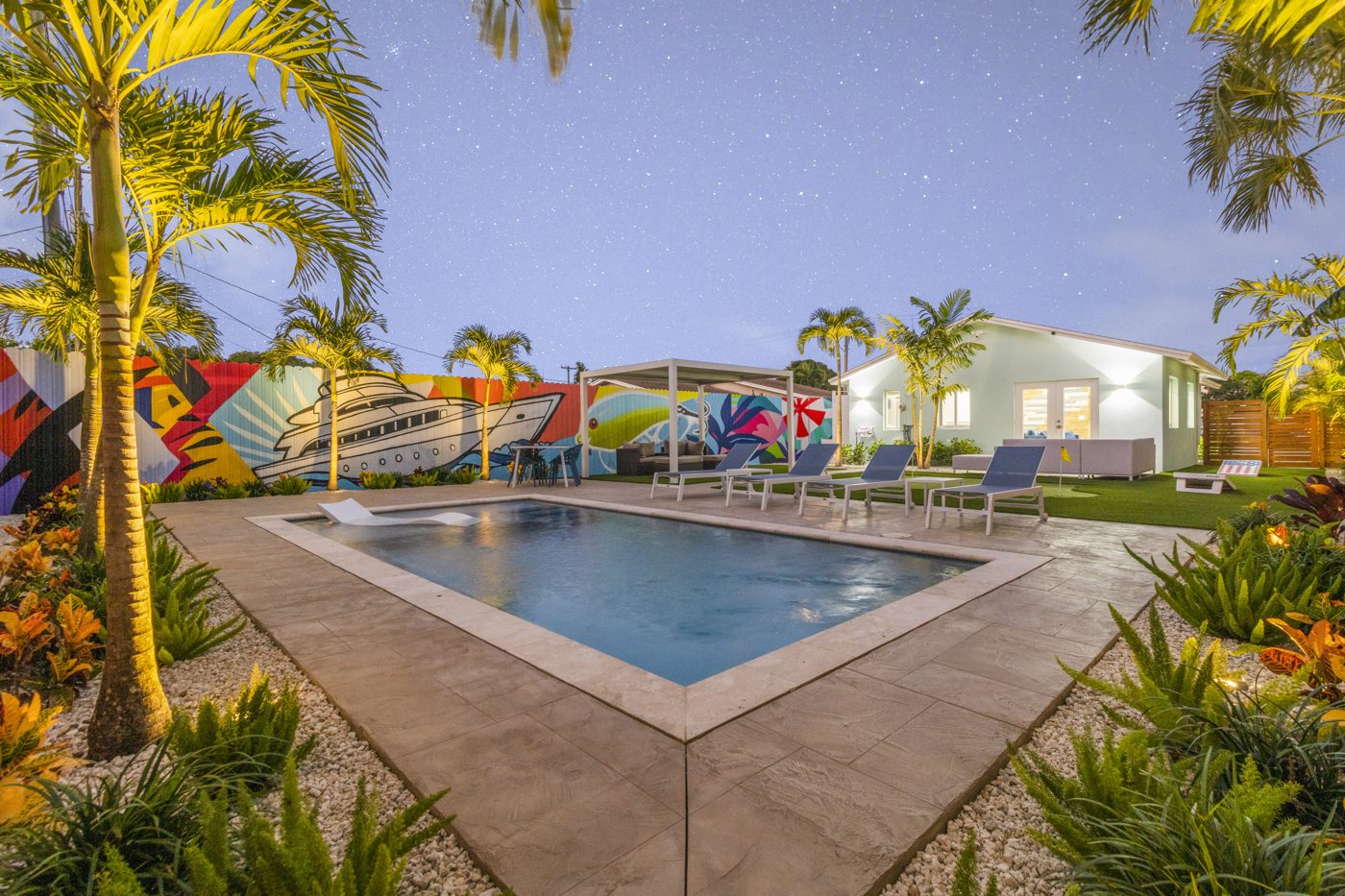 Pool and backyard lit at twilight with the murals glowing behind