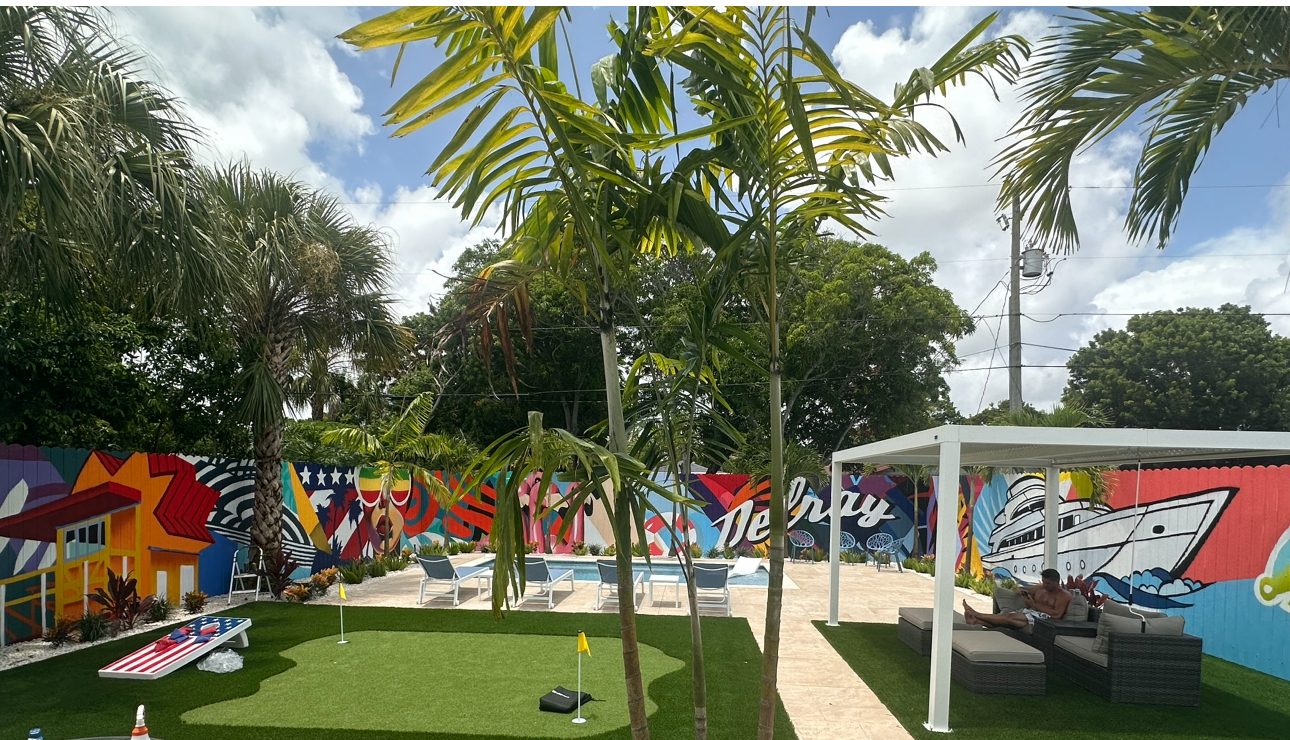 Putting green, cornhole boards and pergola lounge in front of the mural wall by day