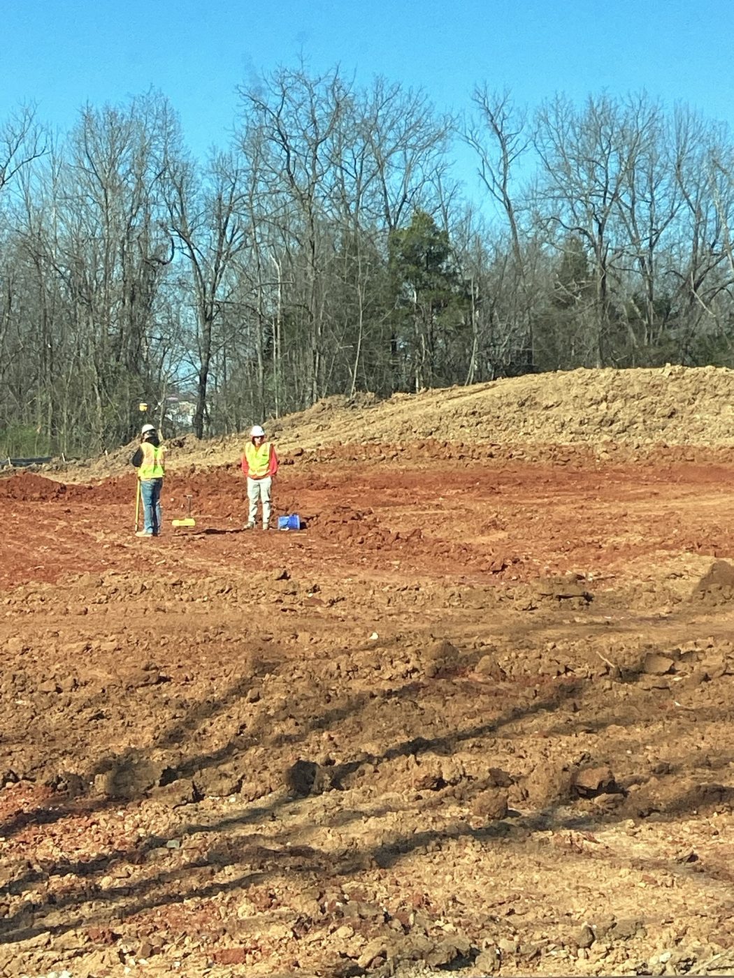 Crew on the graded red clay pad with the excavator behind them