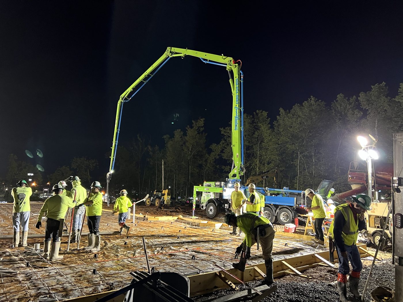 Night concrete pour with the pump truck boom overhead and crew under work lights