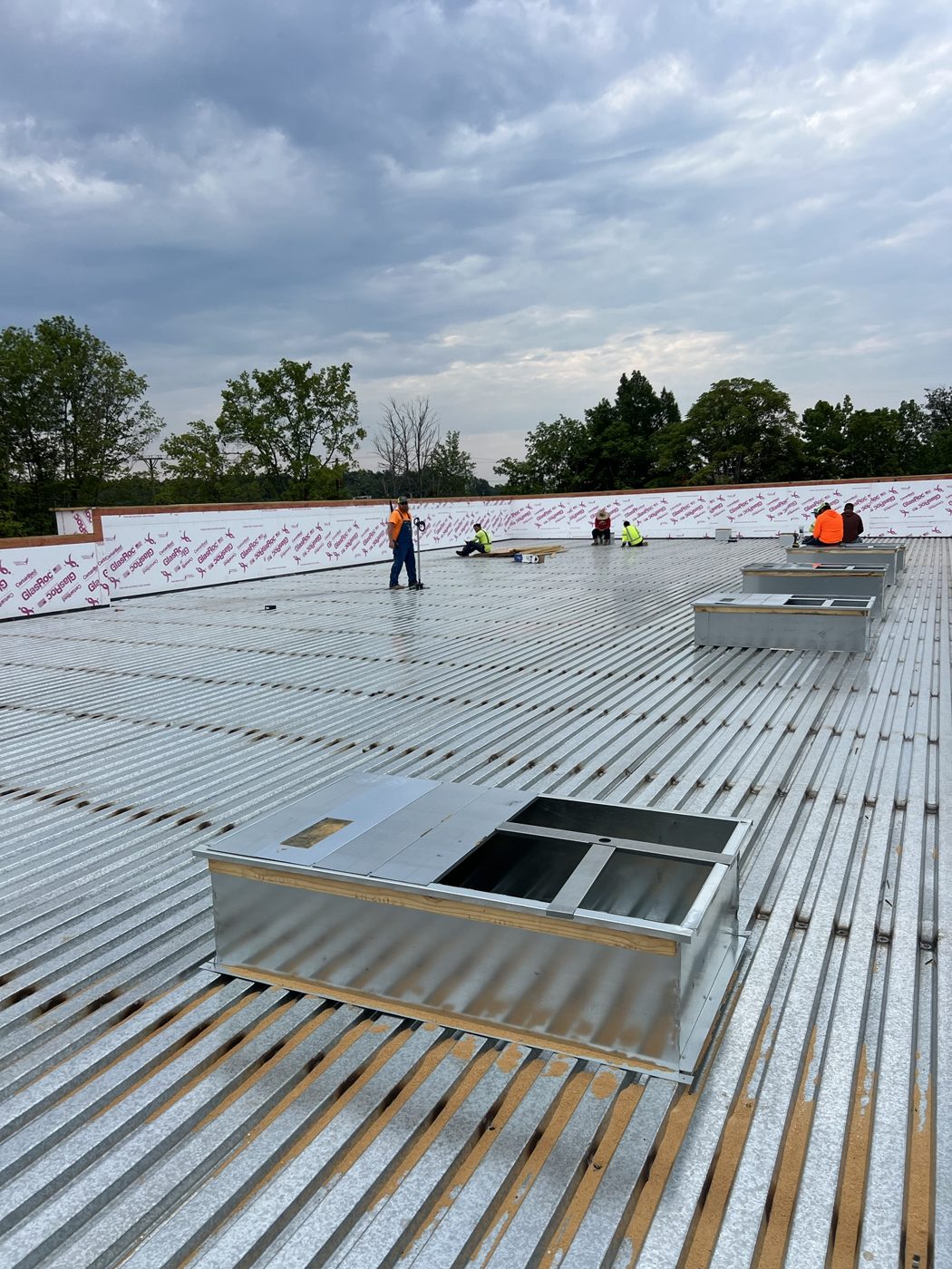 Roofers on the TPO roof beside a rooftop unit curb