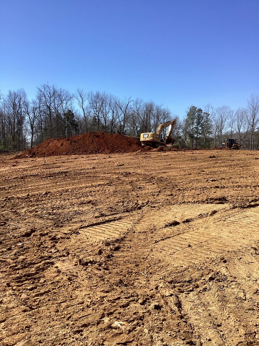 Lot cleared and rough graded, excavator at the tree line