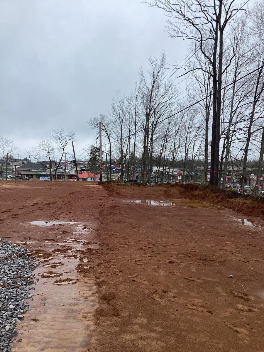 Graded red clay pad after rain, tree line beyond
